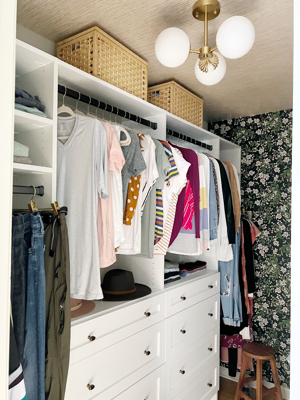 closet makeover after picturing closet built-ins with hanging space and drawers, floral wallpaper on back wall and grasscloth wallpaper on ceiling, baskets on shelves and a semi-flush light fixture